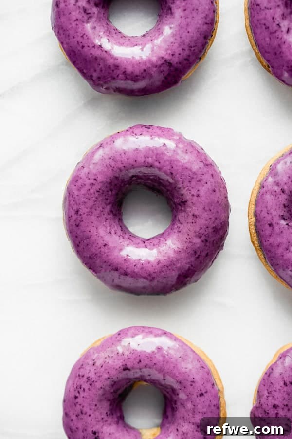 Blueberry Bliss Vegan Donuts 2 Freshly baked vegan blueberry donuts with a vibrant blueberry glaze, artfully arranged on a marble board, ready to be enjoyed.