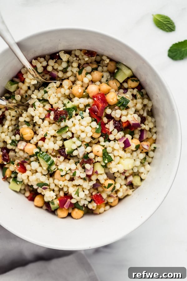 Israeli couscous salad in a large bowl with serving spoons, ready to be enjoyed