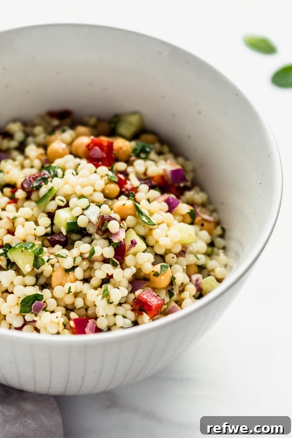 A close-up shot of Israeli couscous salad with chickpeas, vibrant vegetables, and glistening dressing