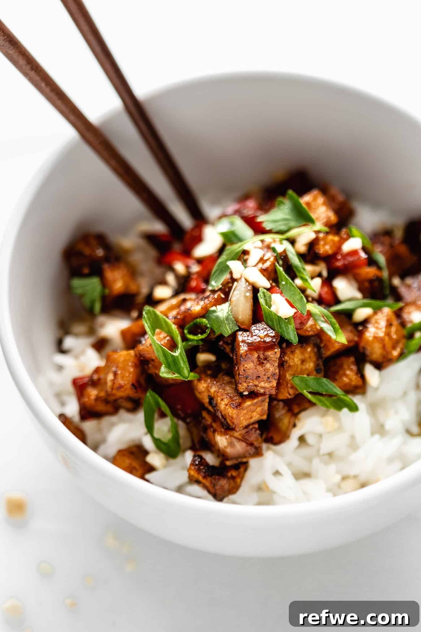 Effortless Kung Pao Tofu 8 A close-up shot of Kung Pao Tofu served elegantly over white rice in a pristine white bowl, garnished with green onions and peanuts.