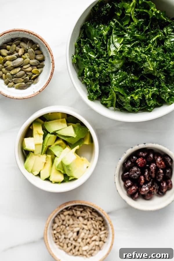 Perfectly Tender Massaged Kale Salad 3 Ingredients for a massaged kale salad laid out: fresh kale, a ripe avocado, bright dried cranberries, and crunchy pumpkin seeds.