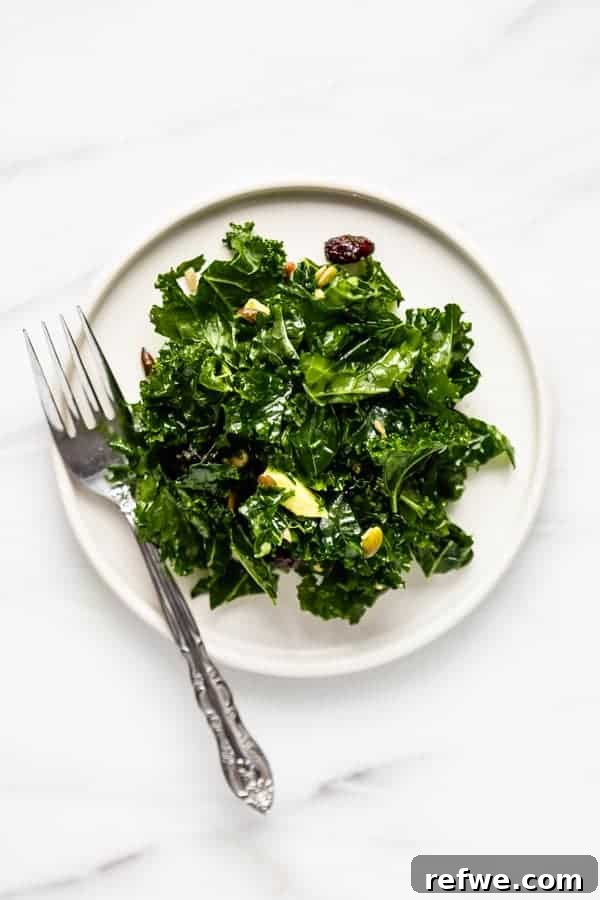 Perfectly Tender Massaged Kale Salad 7 A single plate of massaged kale salad, garnished with avocado slices, pumpkin seeds, and cranberries, ready to be eaten.
