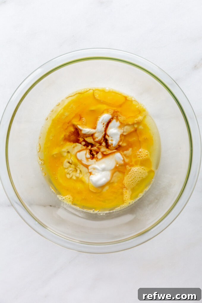 Wholesome Lemon Poppy Seed Delights 3 A bowl containing whisked eggs, Greek yogurt, milk, lemon juice, avocado oil, and vanilla extract.