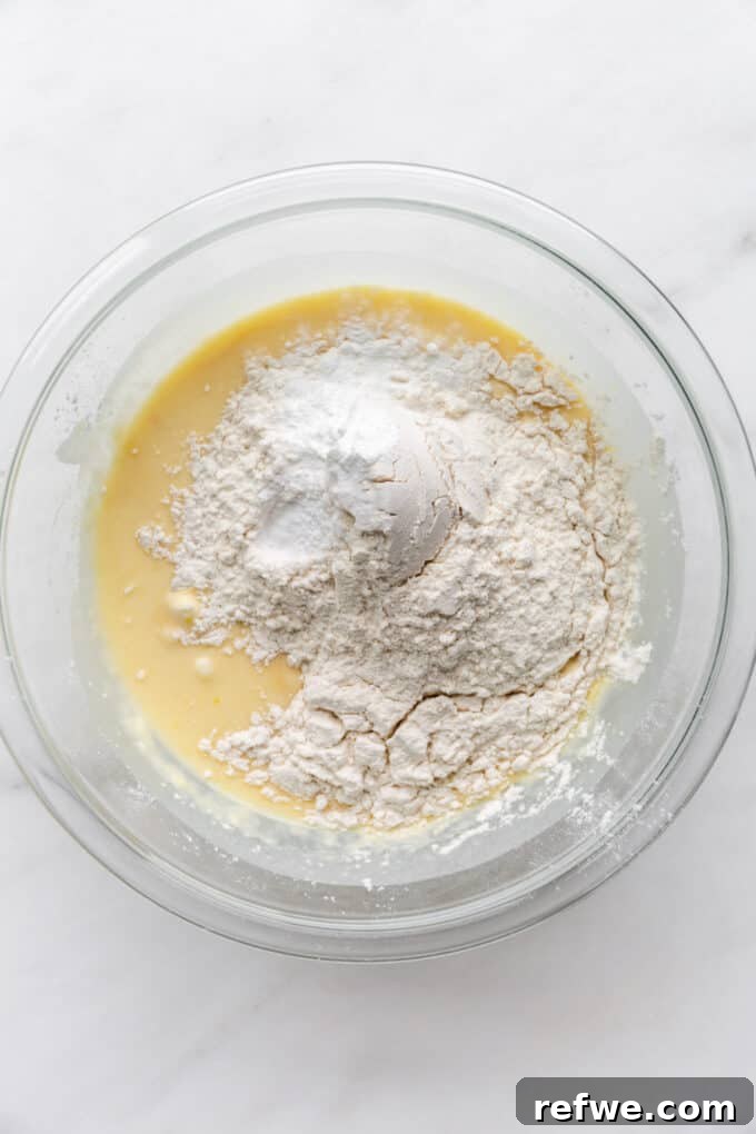 Wholesome Lemon Poppy Seed Delights 6 Dry ingredients (flour, baking powder, baking soda, salt) added to the wet mixture in a mixing bowl.