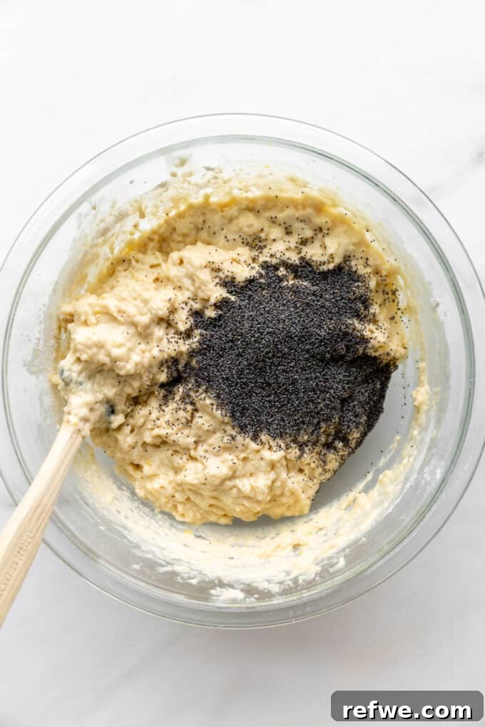 Wholesome Lemon Poppy Seed Delights 7 Poppy seeds being added to the lemon muffin batter in a mixing bowl.