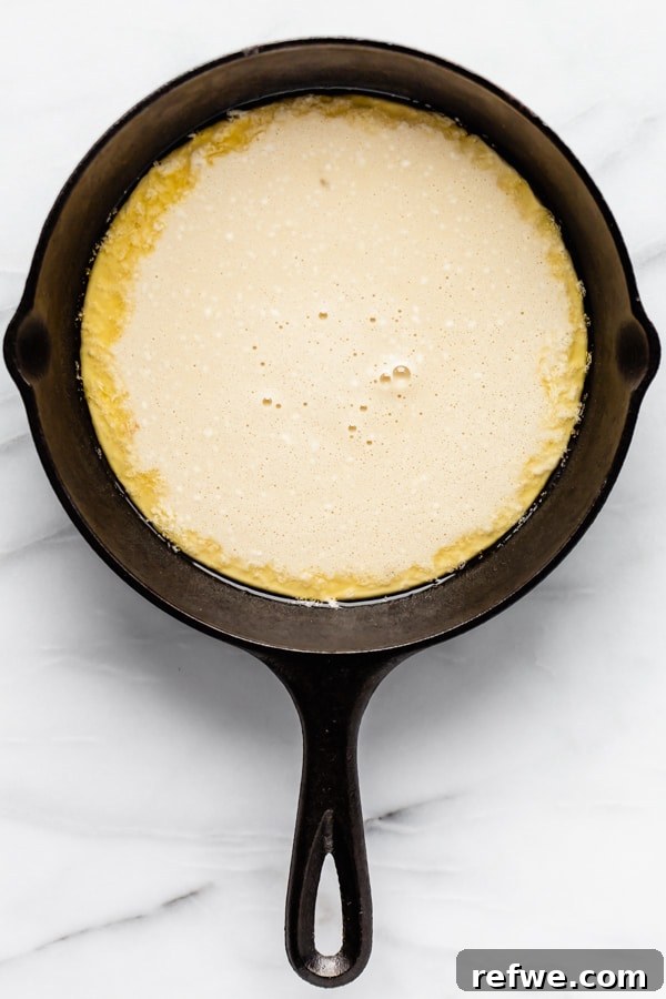 Puffed Skillet Pancake 4 Smooth, golden Dutch Baby Pancake batter perfectly poured into a sizzling, butter-coated cast iron skillet, ready to go into the oven.