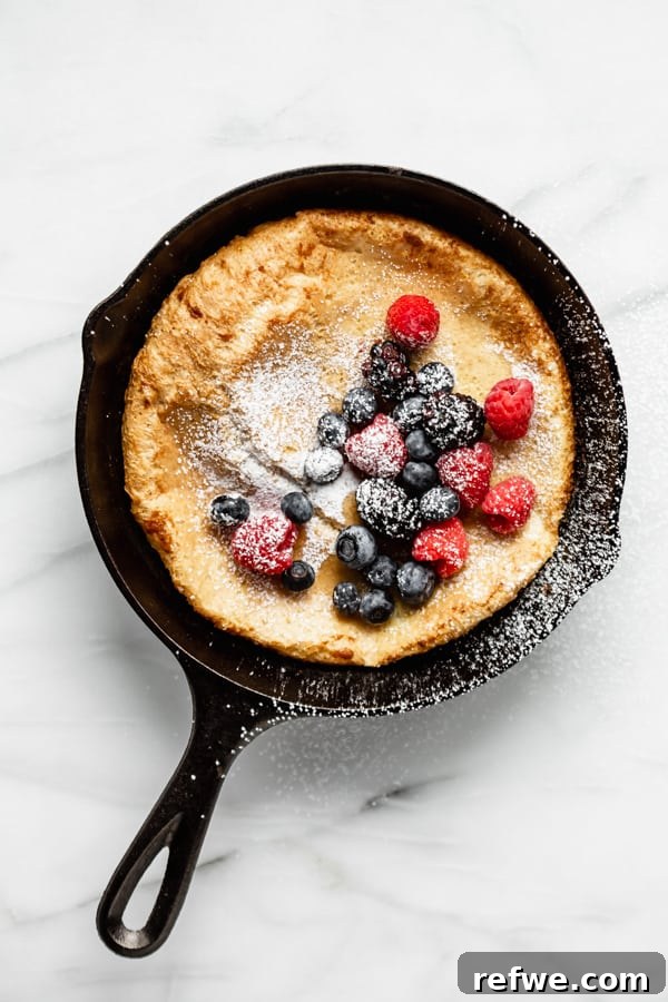Puffed Skillet Pancake 6 A magnificent Dutch Baby Pancake, freshly baked and towering in its cast iron skillet, generously topped with a medley of fresh berries and a delicate dusting of powdered sugar.