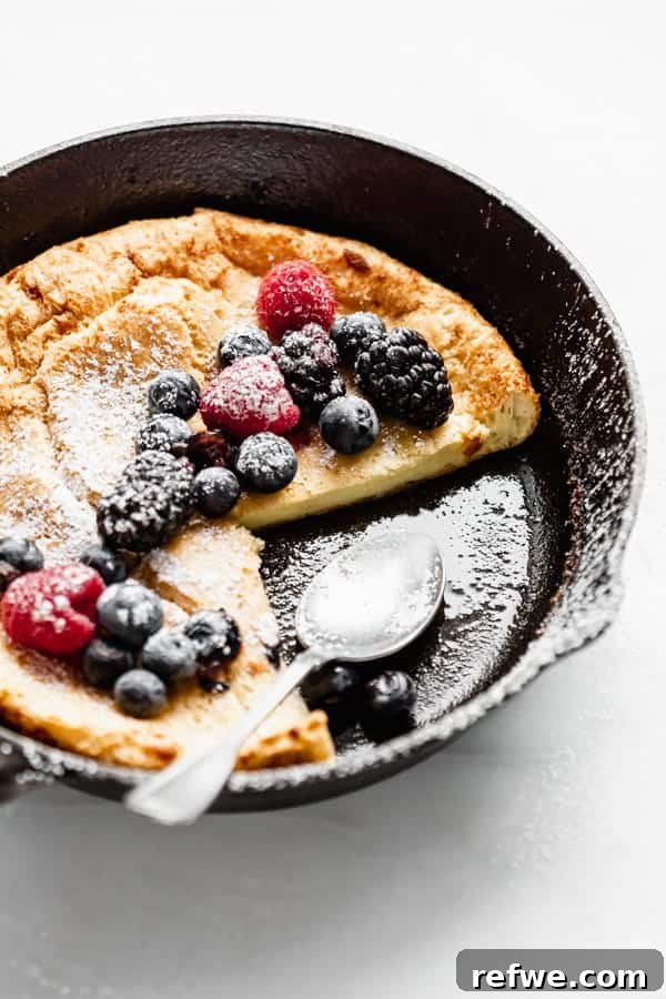 Puffed Skillet Pancake 7 A close-up view of the golden, airy interior and crispy edges of a freshly baked Dutch Baby Pancake in a cast iron skillet, with a serving spoon poised.
