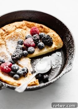 A golden Dutch Baby Pancake in a cast iron skillet, garnished with fresh berries.