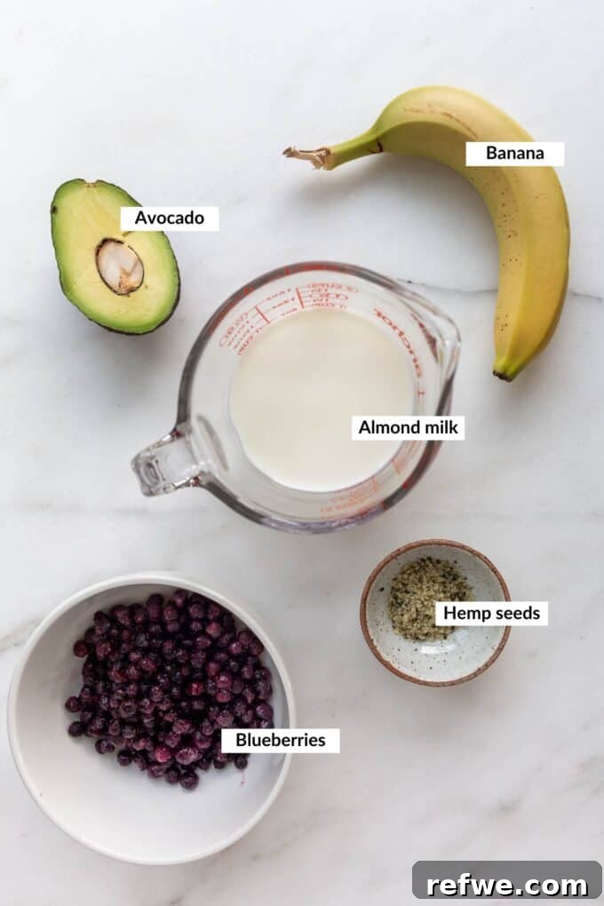 Velvety Blueberry Avocado Blend 3 A flat lay of fresh blueberries, a ripe avocado, a frozen banana, almond milk, and hemp seeds laid out for a smoothie.