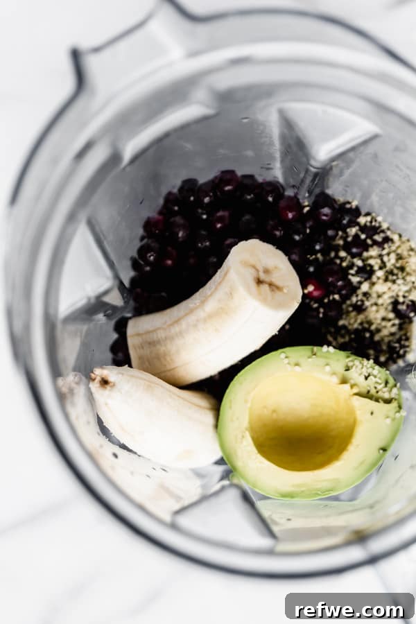 Velvety Blueberry Avocado Blend 4 All ingredients for the blueberry avocado smoothie, including almond milk, blueberries, avocado, banana, and hemp seeds, are added to a high-speed blender container.