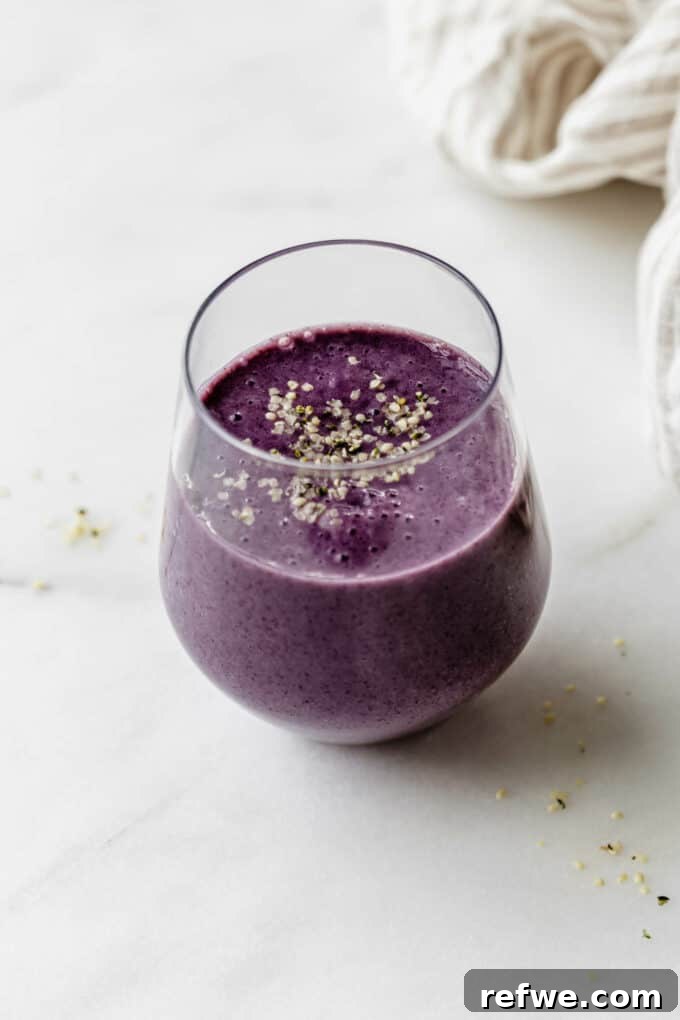 Velvety Blueberry Avocado Blend 6 A beautifully presented glass of blueberry avocado smoothie, garnished with fresh berries and mint, resting on a stylish marble board.