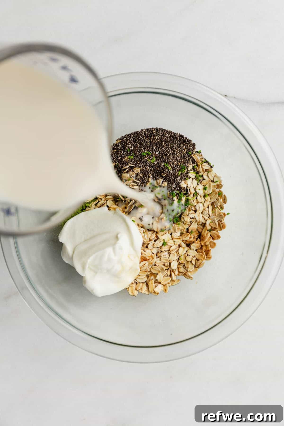 Key Lime Pie Overnight Oats Recipe for Creamy Citrus Breakfast 5 Milk being poured into a bowl of oats, yogurt and chia seeds.