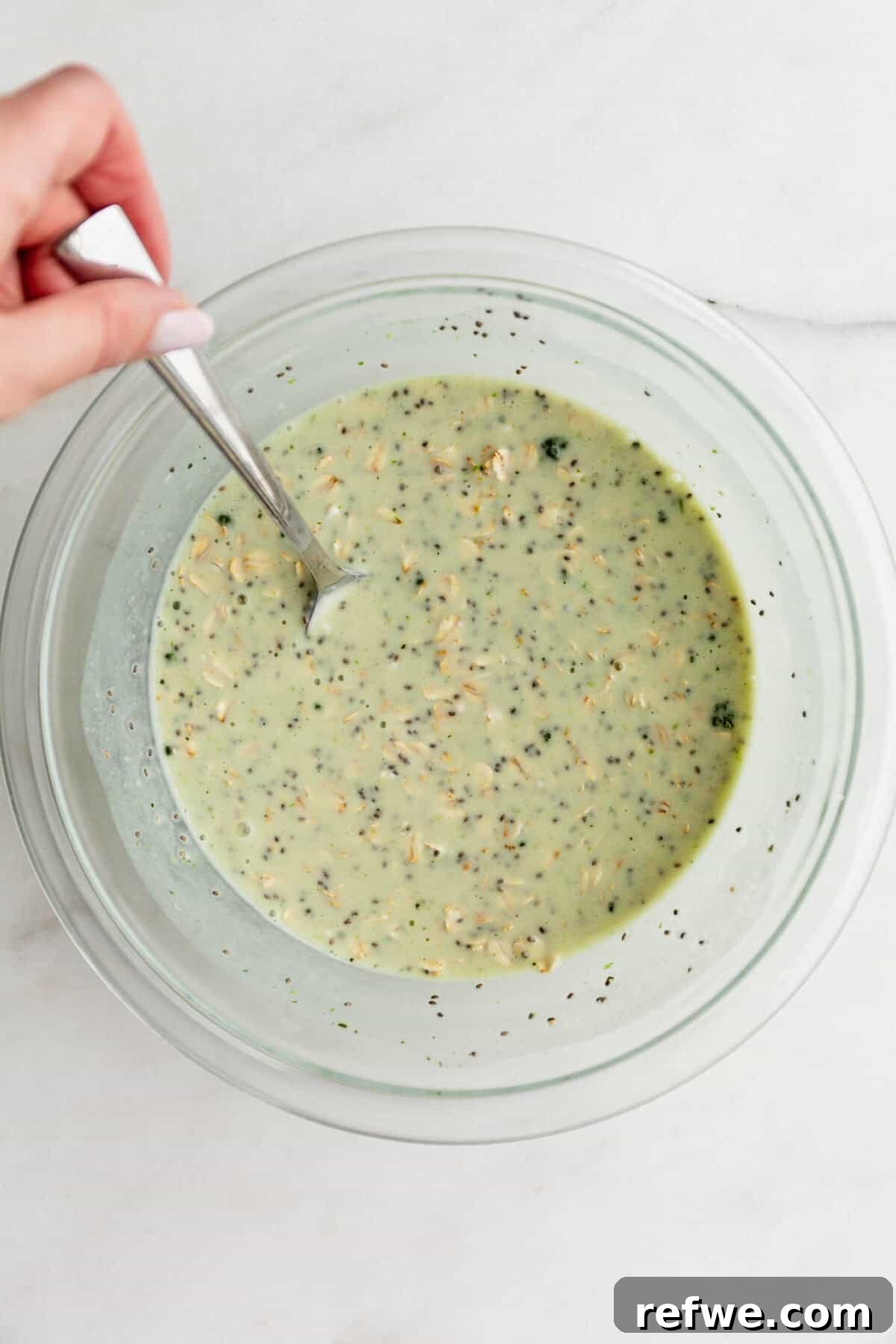 Key Lime Pie Overnight Oats Recipe for Creamy Citrus Breakfast 6 a spoon mixing lime overnight oats in a clear mixing bowl.