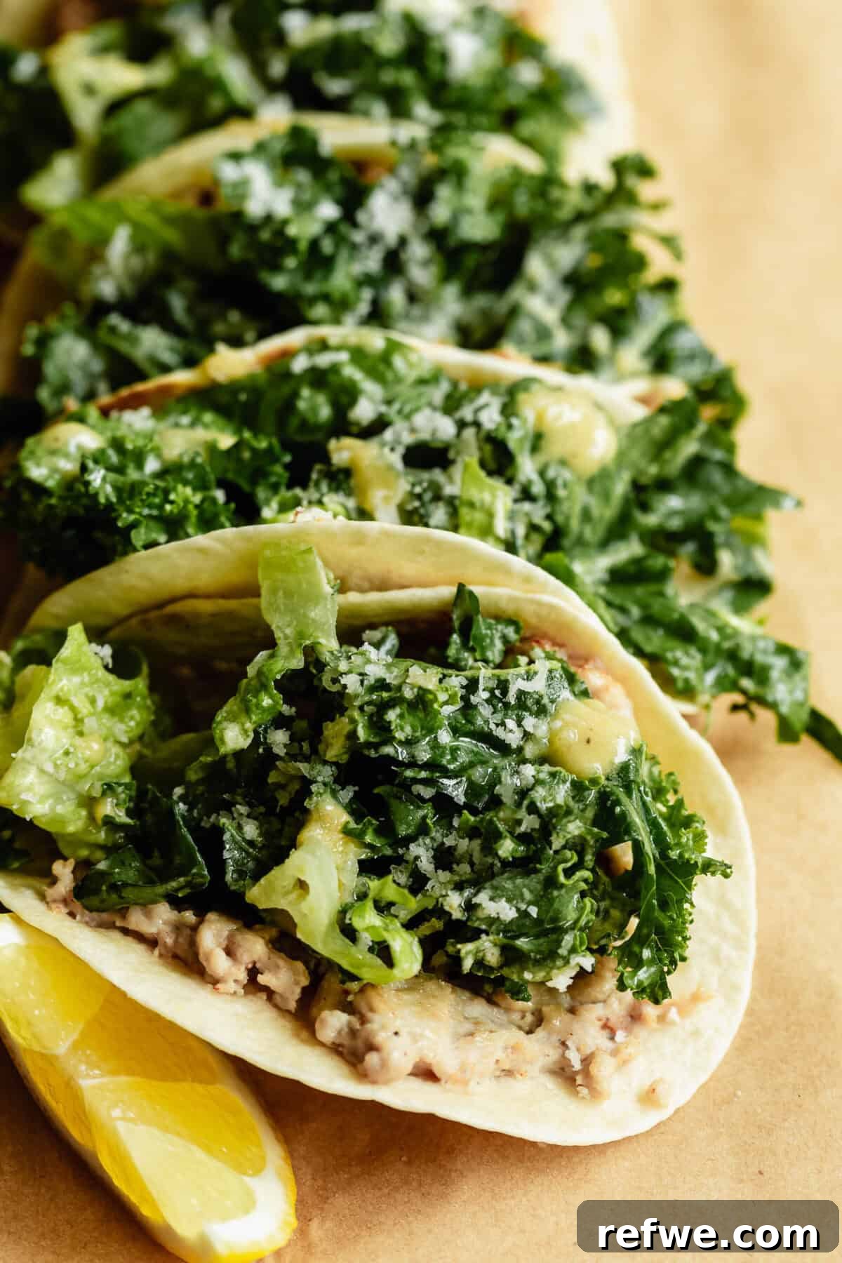 Close-up of chicken caesar smashed tacos loaded with kale caesar salad and parmesan, served with lemon wedges on kraft paper.