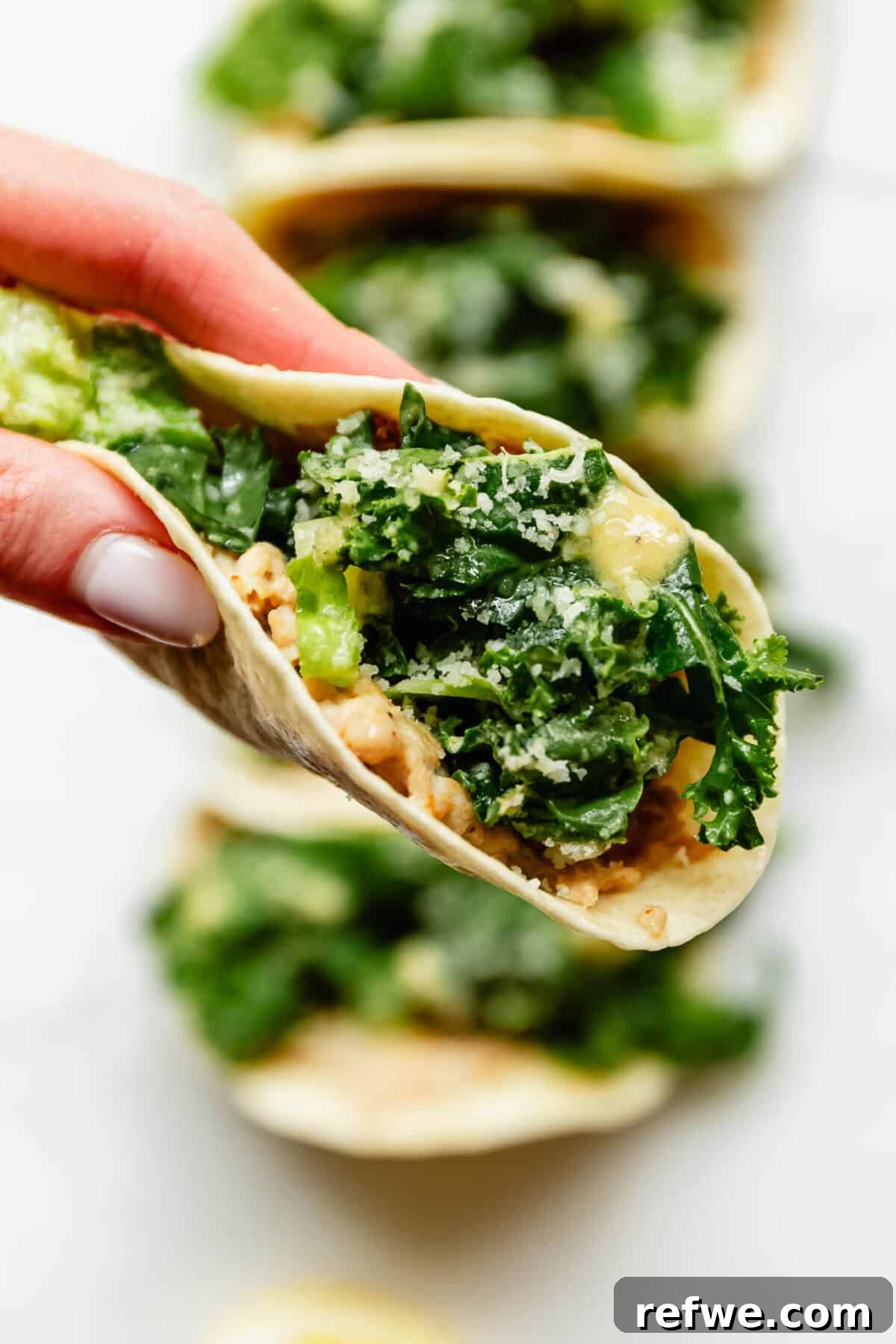 Hand holding a chicken caesar smashed taco filled with kale caesar salad and parmesan cheese.