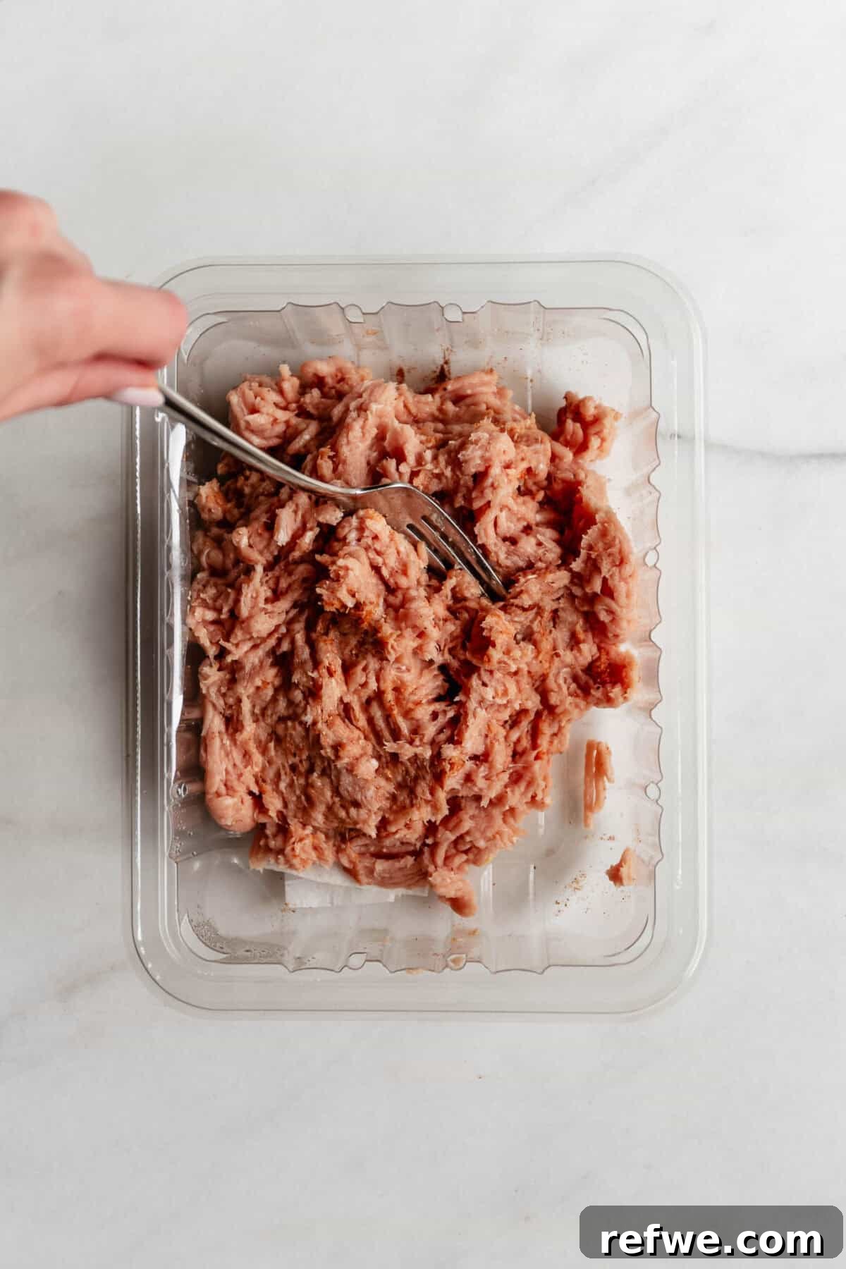 Hand mixing seasoned ground chicken in a plastic container with a fork to prepare for chicken caesar smashed tacos.
