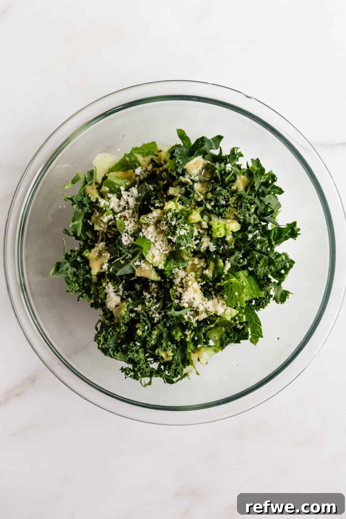 Kale caesar salad with parmesan cheese in a glass bowl viewed from above, topping for chicken caesar smashed tacos.
