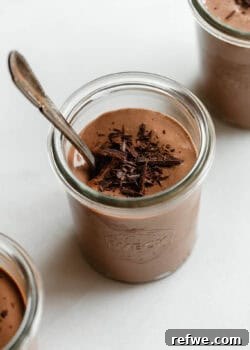 Greek yogurt chocolate mousse served in glass jars topped with chocolate shavings and a spoon.
