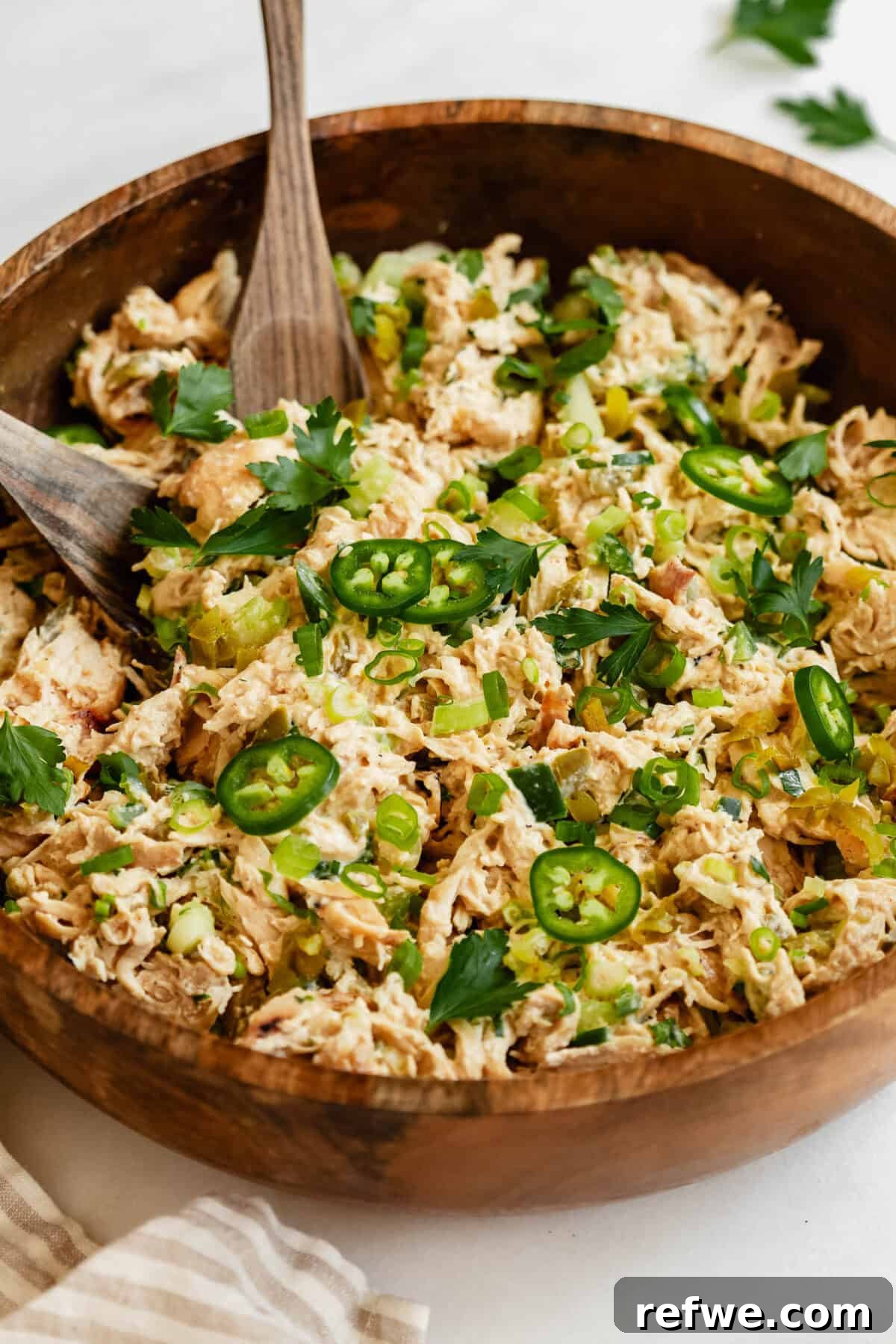 Jalapeño Popper Chicken Salad Recipe — Creamy, Spicy Lunch Idea 2 A close-up of jalapeno popper chicken salad in a wooden bowl, topped with sliced jalapeños, green onions, and fresh herbs.