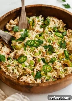 A close-up of jalapeno popper chicken salad in a wooden bowl, topped with sliced jalapeños, green onions, and fresh herbs.