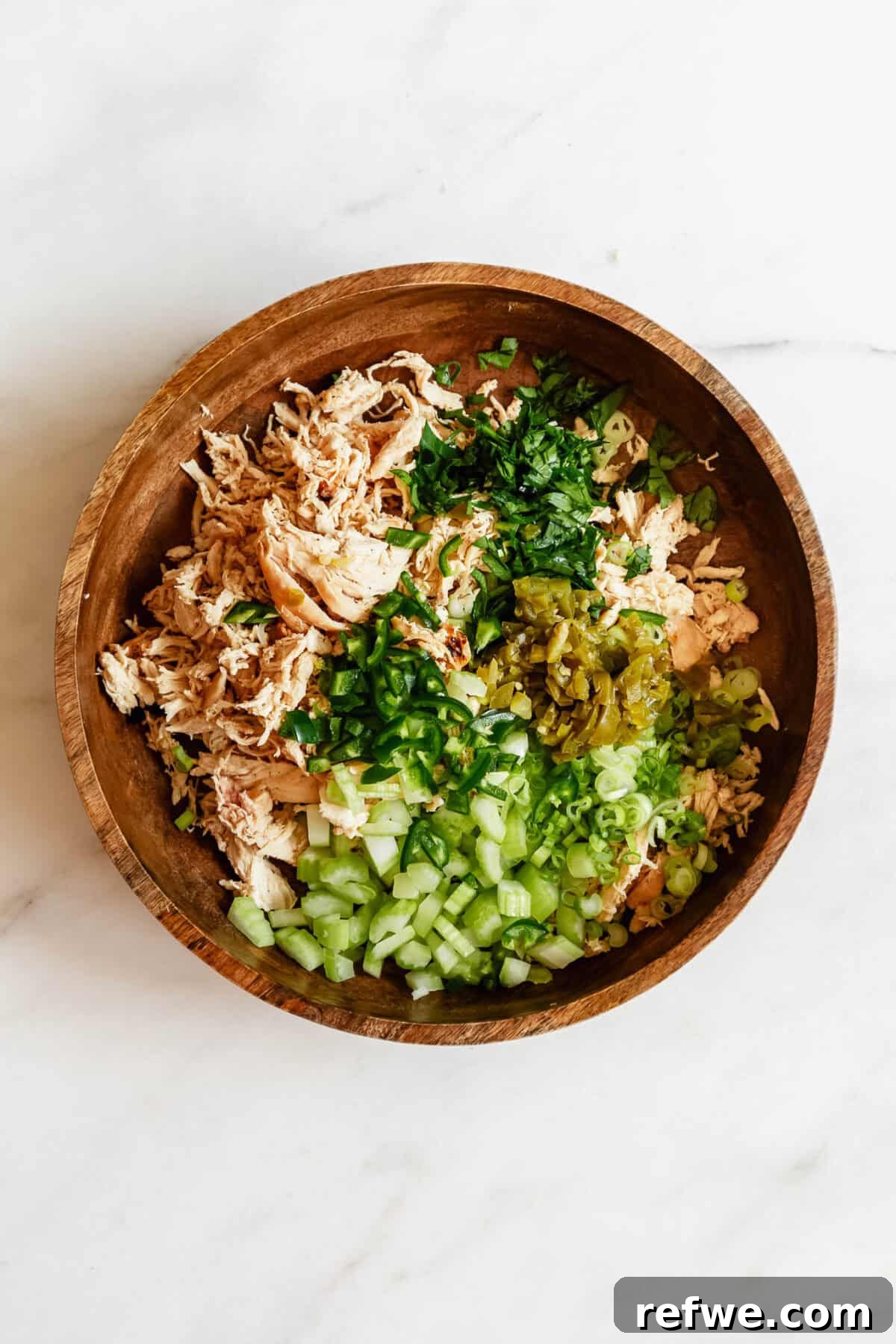 Jalapeño Popper Chicken Salad Recipe — Creamy, Spicy Lunch Idea 6 Overhead view of shredded chicken and chopped celery and green onions in a wooden bowl for jalapeno popper chicken salad.