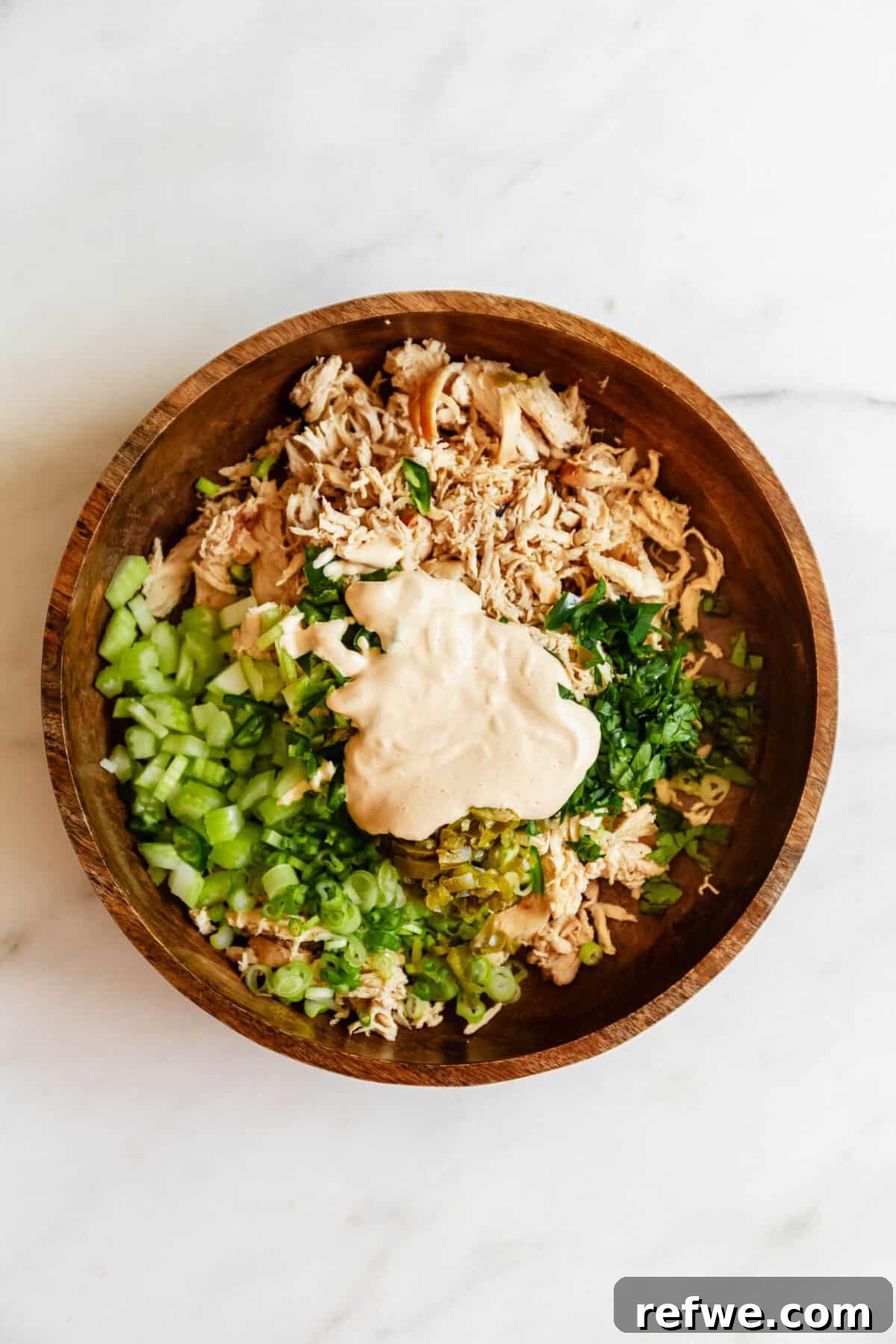Jalapeño Popper Chicken Salad Recipe — Creamy, Spicy Lunch Idea 7 Overhead view of shredded chicken topped with diced green onions and celery in a wooden bowl for jalapeno popper chicken salad.
