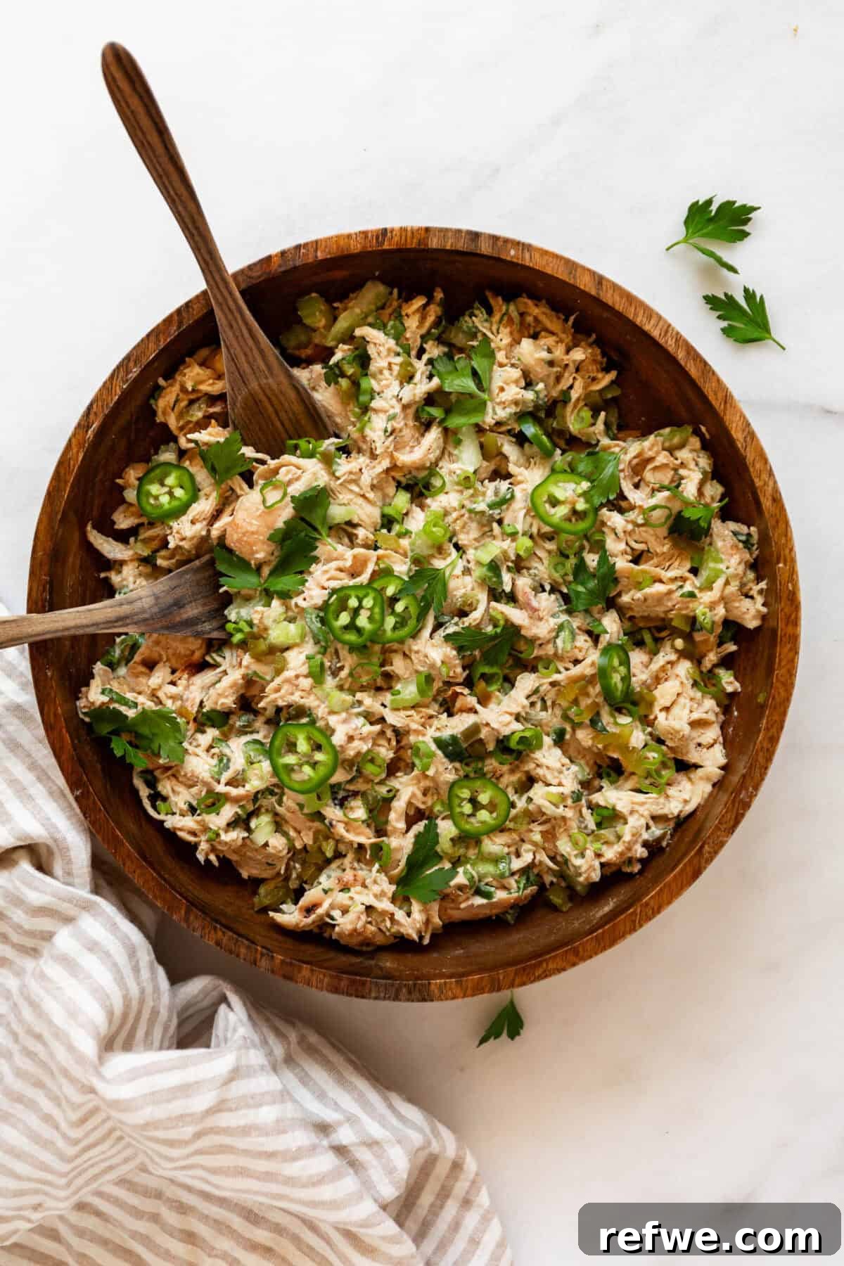 Jalapeño Popper Chicken Salad Recipe — Creamy, Spicy Lunch Idea 9 Overhead view of jalapeno popper chicken salad in a wooden bowl with a wooden spoon, topped with sliced jalapeños and fresh herbs.