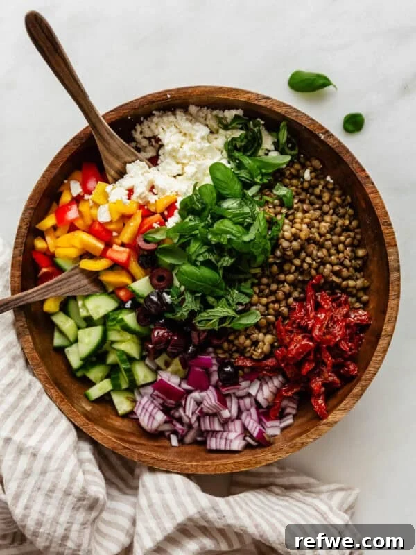 Mediterranean lentil salad in a wood bowl with wood spoons and a napkin on the side.