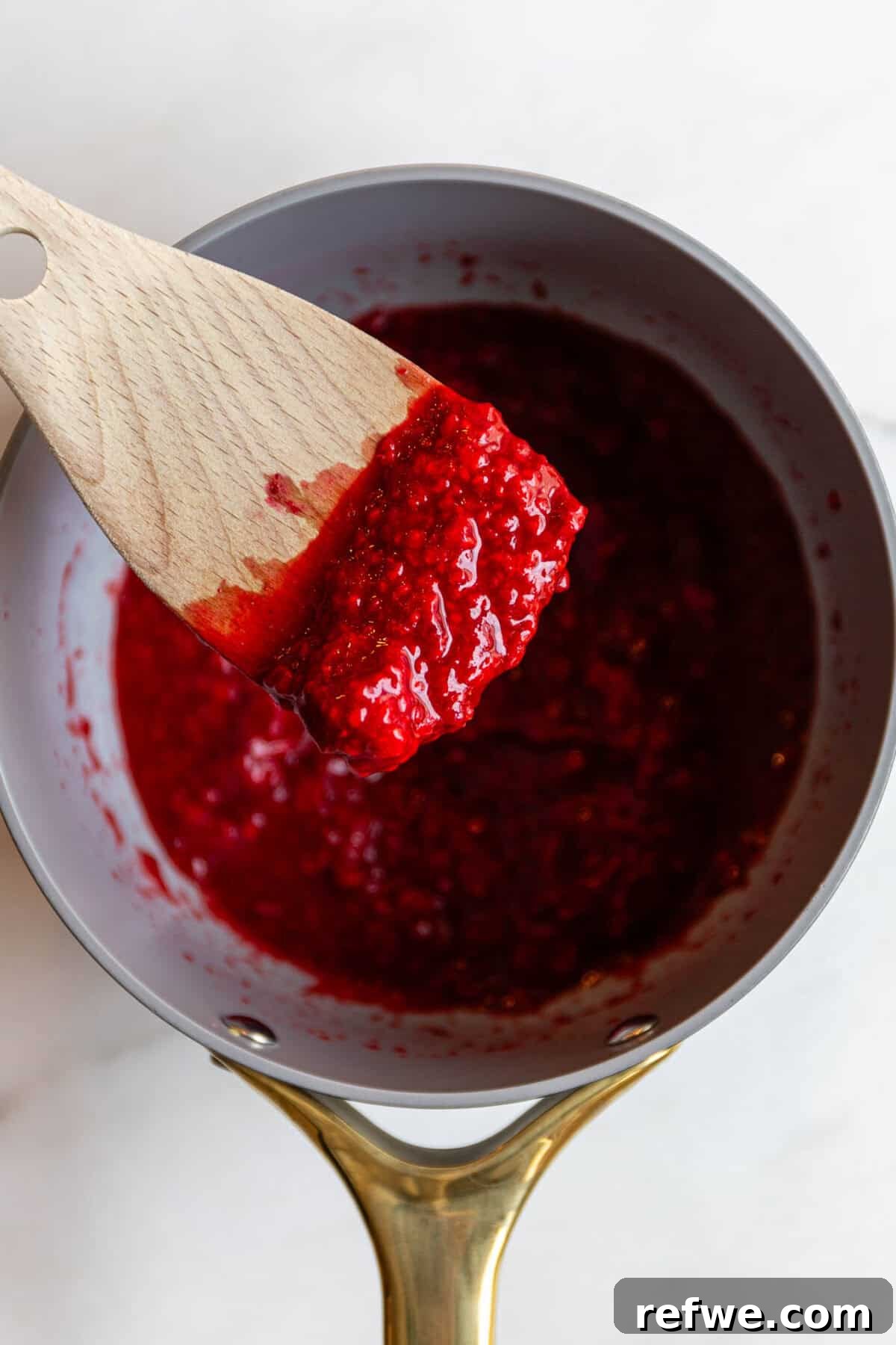 Chocolate Chia Jam Energy Bites: No-Bake Snack Recipe 5 Raspberry chia seed jam being scooped with a wooden spatula in a saucepan.