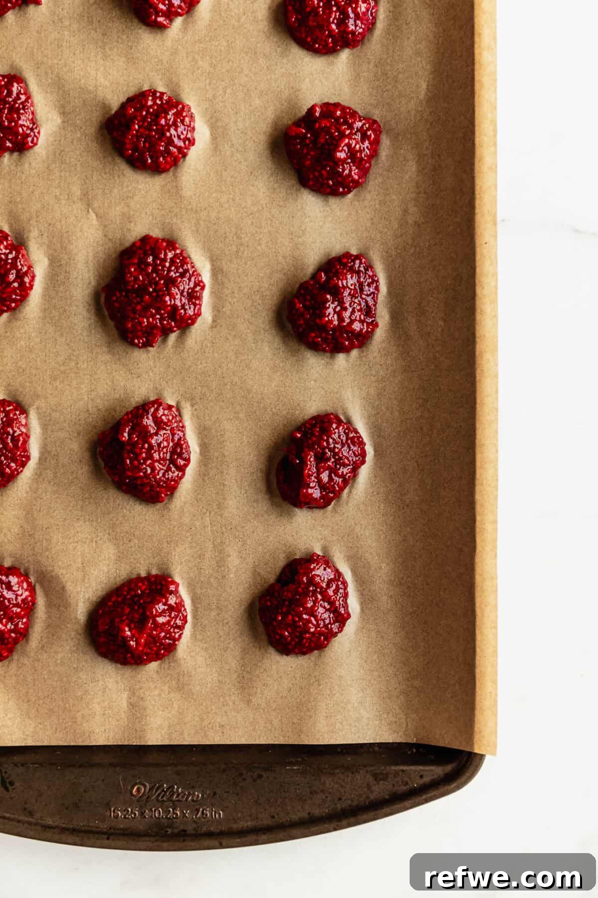 Chocolate Chia Jam Energy Bites: No-Bake Snack Recipe 6 Raspberry chia seed jam bites rolled into balls and placed on parchment paper on a baking sheet.