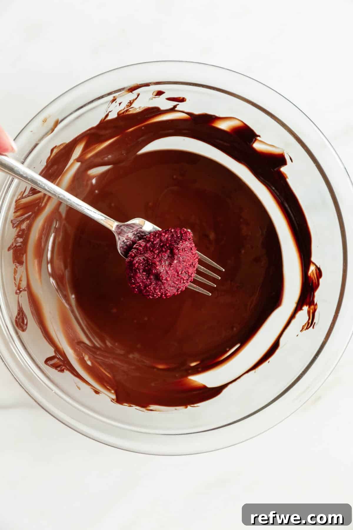 Chocolate Chia Jam Energy Bites: No-Bake Snack Recipe 8 a frozen raspberry chia jam bite on a fork above a bowl of dark chocolate.