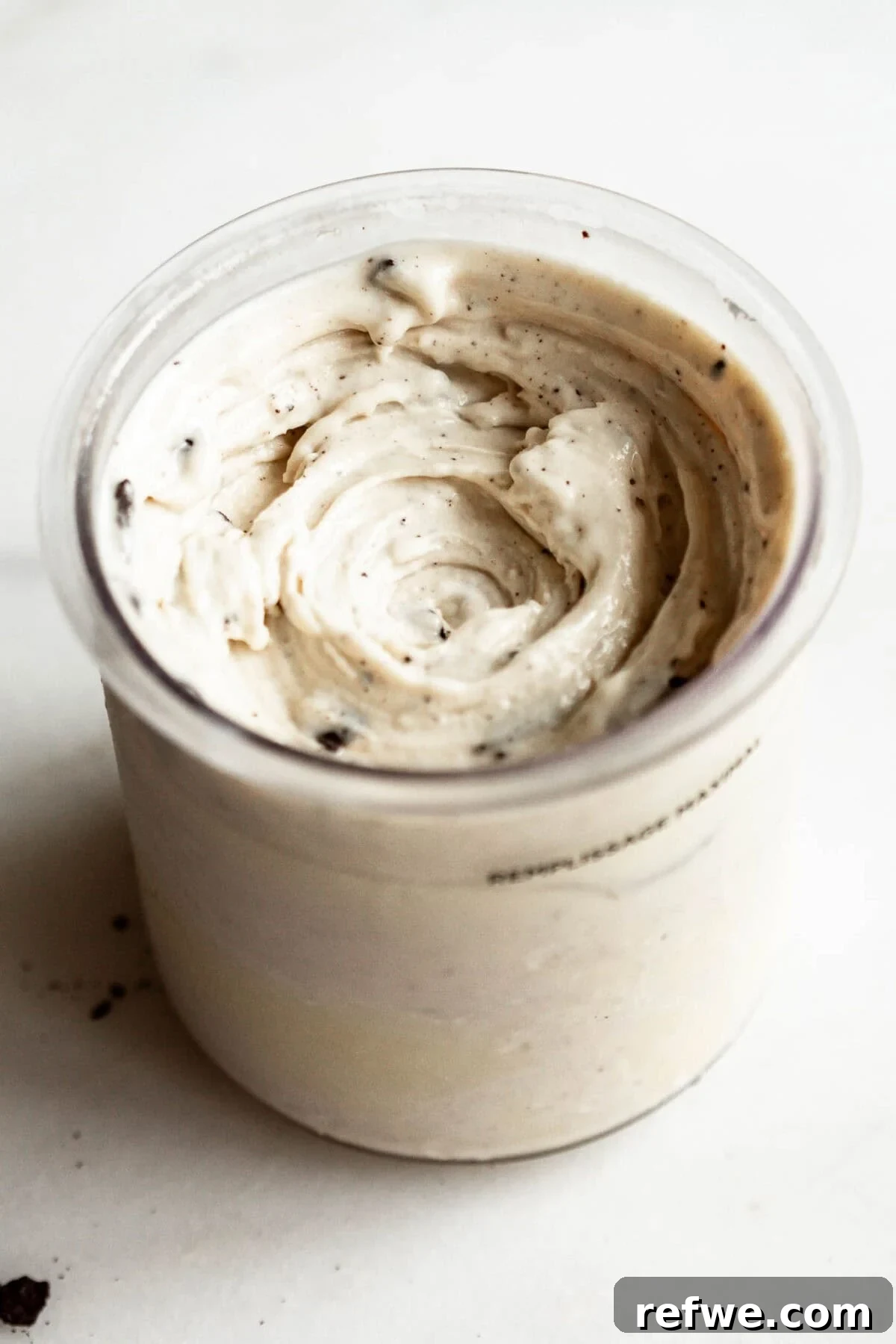 High-Protein Cookies & Cream Recipe for Ninja Creami Ice Cream 10 Ninja Creami container filled with finished cookies and cream ice cream, showing swirled creamy texture with Oreo cookie bits mixed throughout.