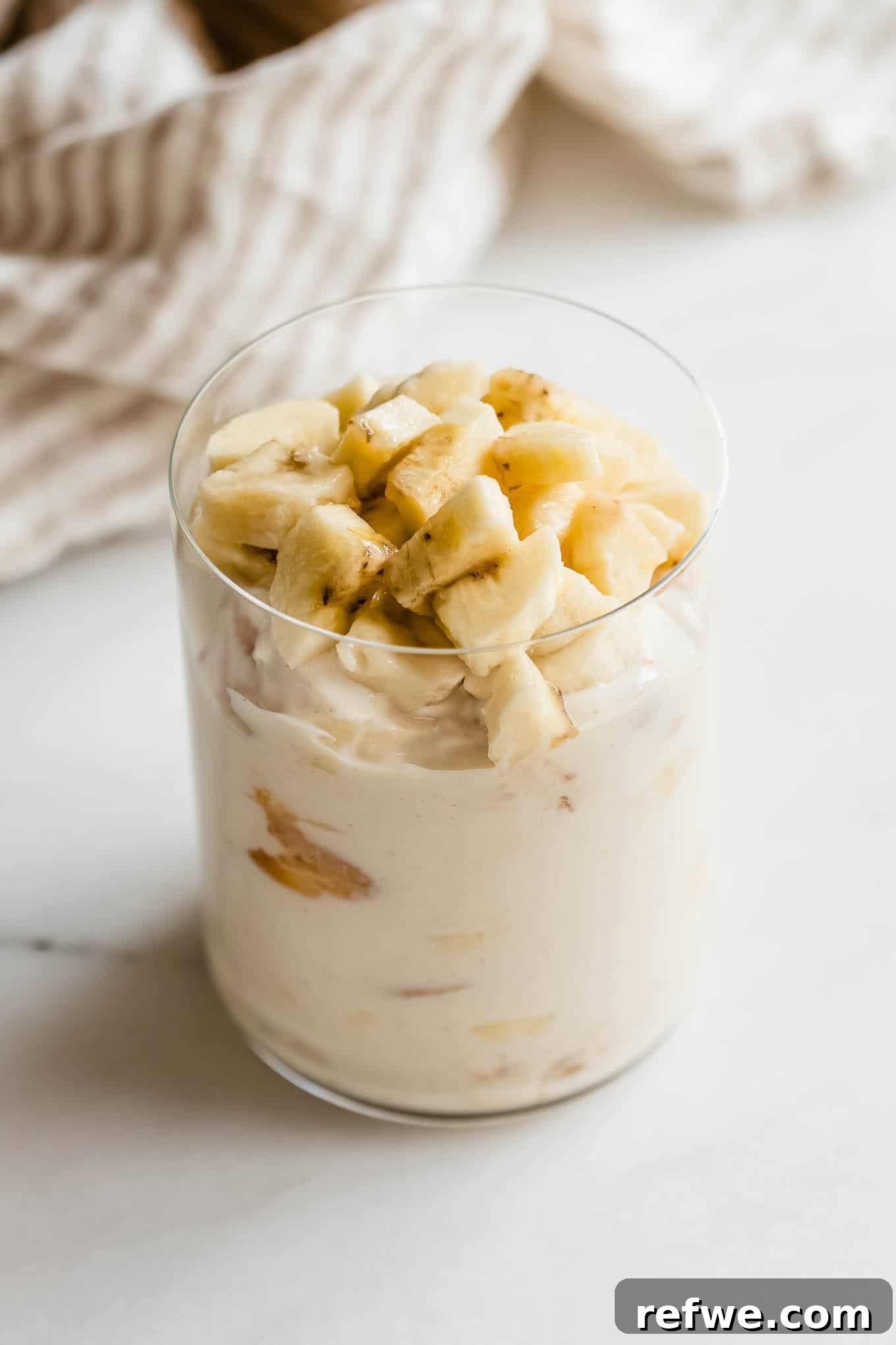 High-Protein Banana Yogurt Pudding Recipe with Greek Yogurt 9 Tall glass jar of high protein banana pudding topped with banana slices.