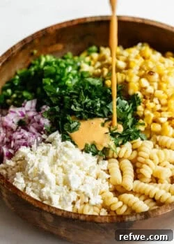 dressing being poured into a bowl of elote pasta salad.