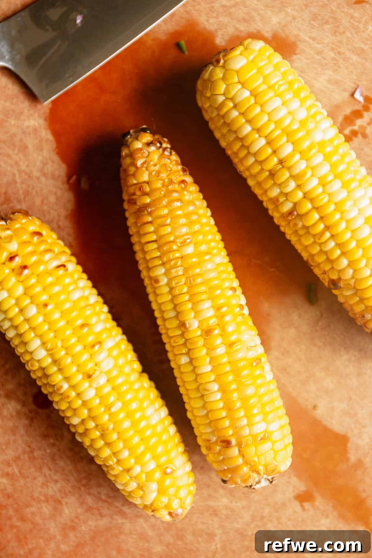 three ears of corn on a wood cutting board.