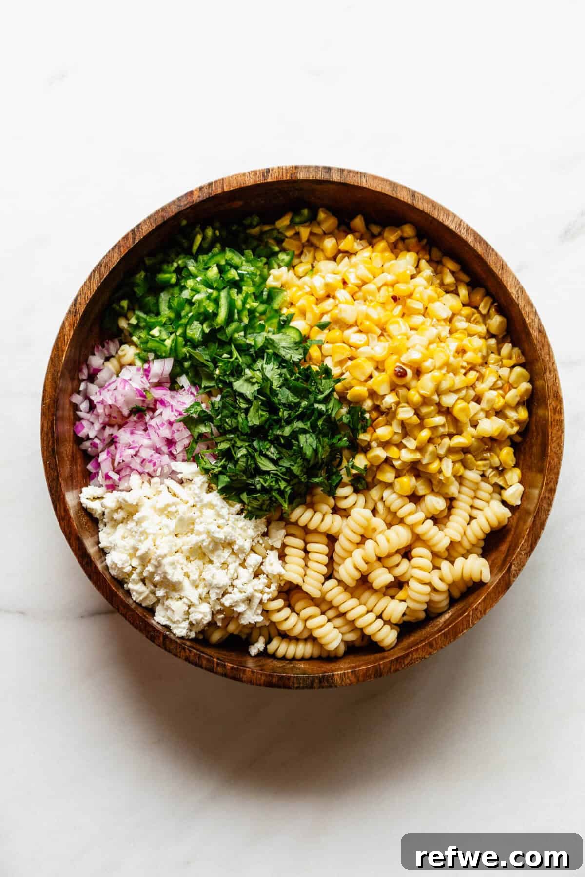 pasta, corn, contija cheese, red onion, jalapeno and cilantro in a wood bowl.