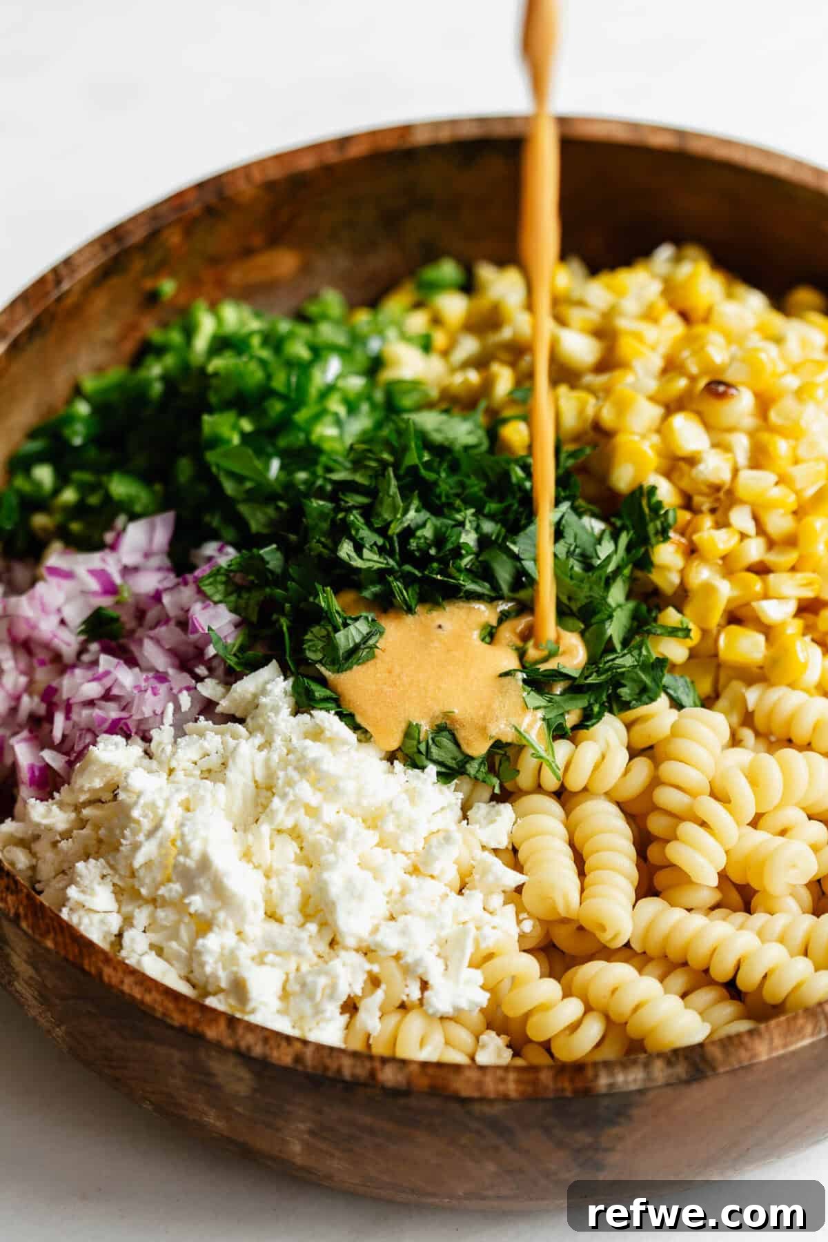 dressing being poured into a bowl of elote pasta salad.