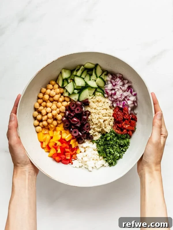 two hands holding a mixing bowl with ingredients for a quinoa salad