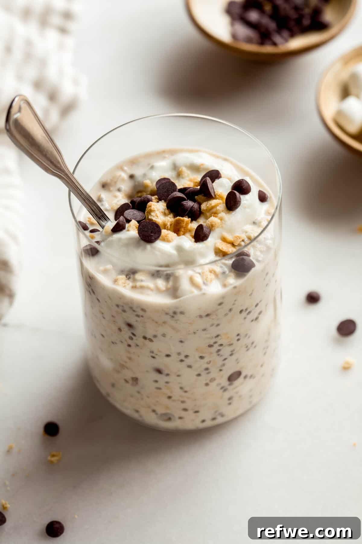 S'mores Overnight Oats with Chocolate and Marshmallow 8 A jar of smores overnight oats topped with graham cracker crumbs and chocolate chips with a spoon in it.