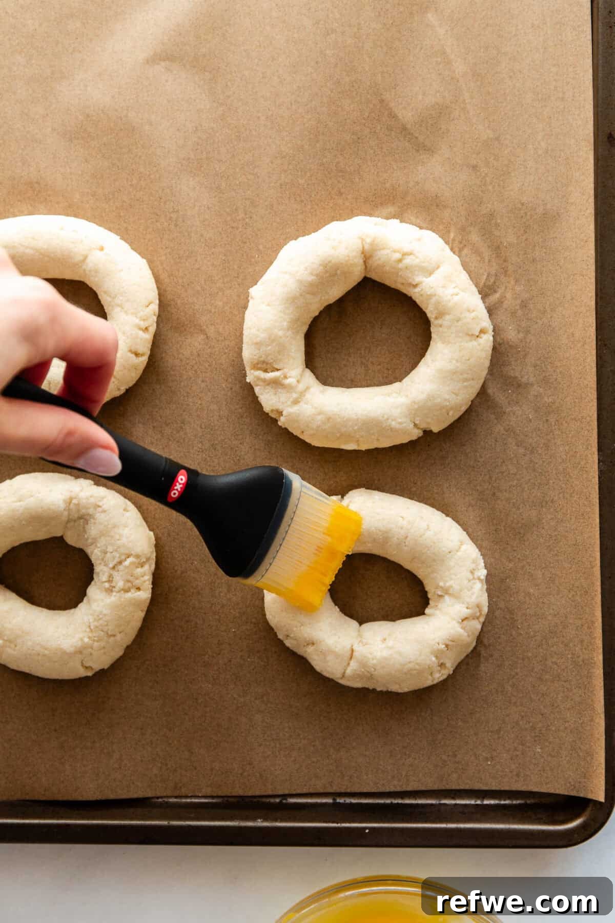 Cottage Cheese and Almond Flour Bagel Recipe 10 A hand brushing egg wash onto unbaked Cottage Cheese Almond Flour Bagels.