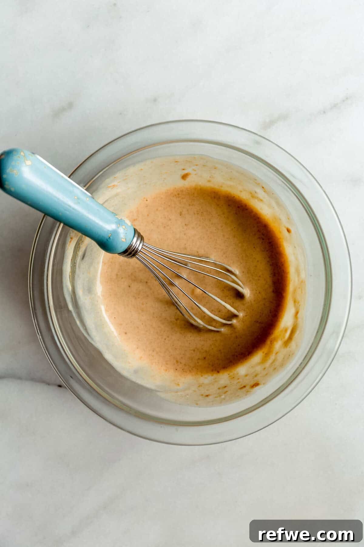 Protein-Packed Cottage Cheese Cookie Dough 4 blended cottage cheese with nut butter maple syrup and vanilla in a clear bowl with a blue whisk.