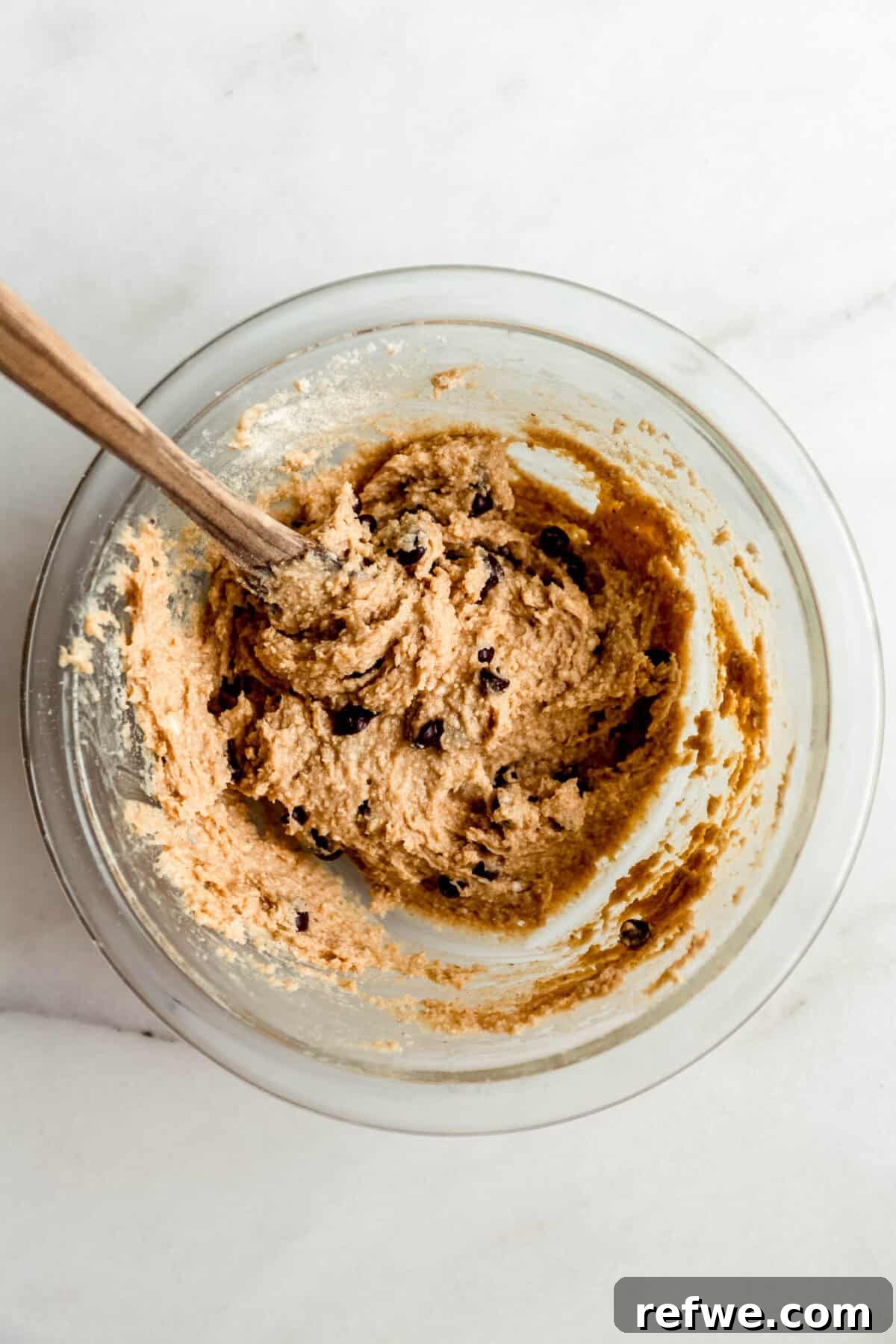 Protein-Packed Cottage Cheese Cookie Dough 6 Cottage cheese cookie dough in a clear mixing bowl with a wood spoon.