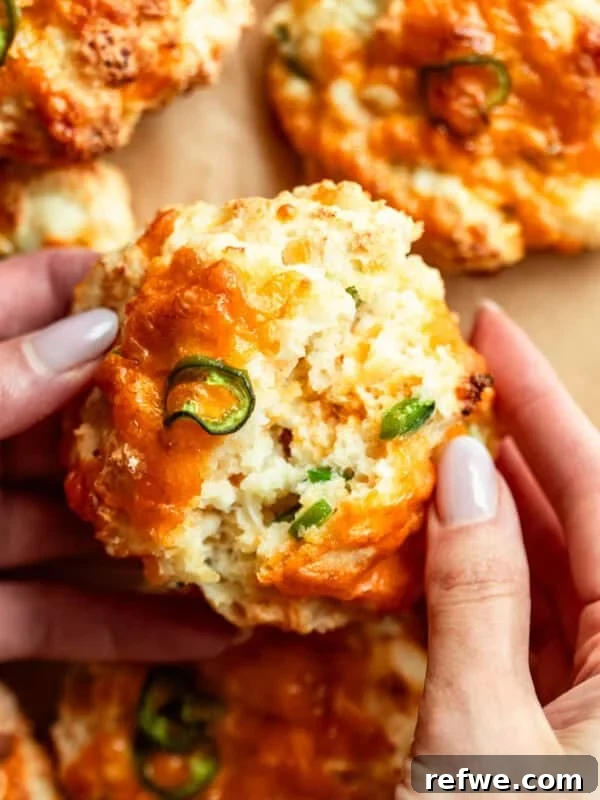 two hands breaking a jalapeno cheddar cottage cheese biscuit in half.