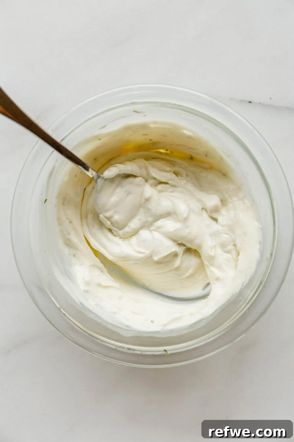 Mini Key Lime Pie Pudding Jars with Greek Yogurt 5 Glass bowl of whipped Greek yogurt mixture with lime zest being stirred with a spoon for key lime pie jars.