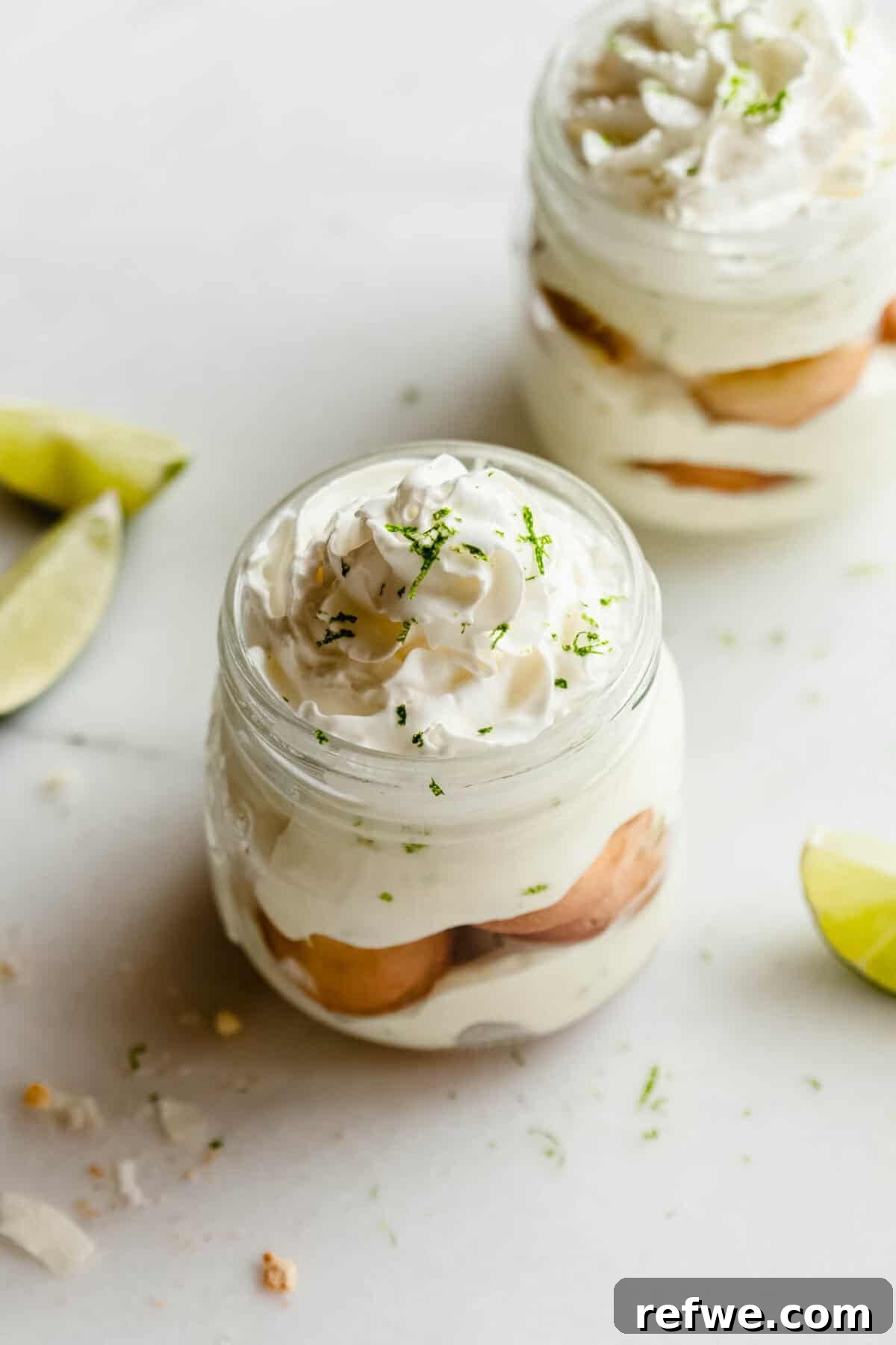 Mini Key Lime Pie Pudding Jars with Greek Yogurt 9 Finished key lime pie jars layered with cookies, Greek yogurt filling, and whipped topping, garnished with lime zest and lime wedges.