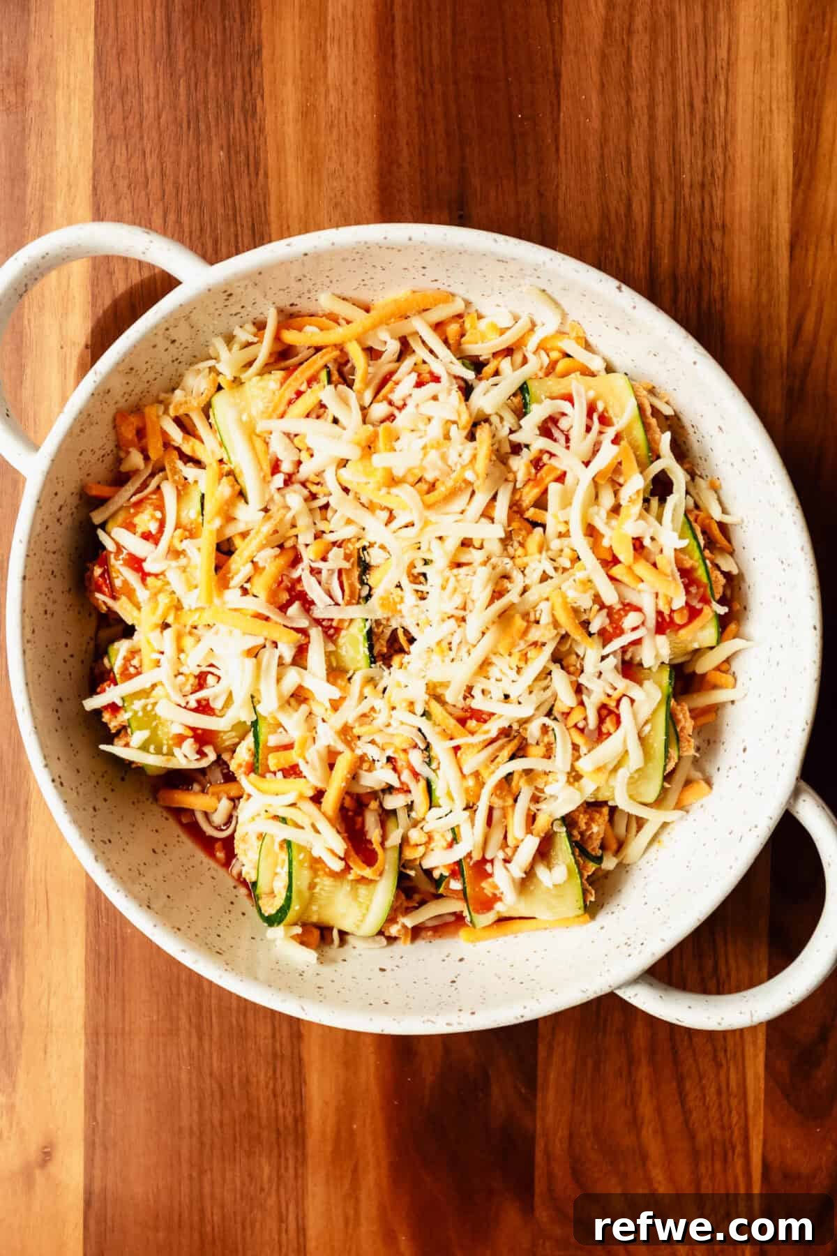 Buffalo Chicken Zucchini Roll-Ups Recipe 11 buffalo chicken zucchini roll ups in a baking dish with hot sauce topped with shredded cheese.