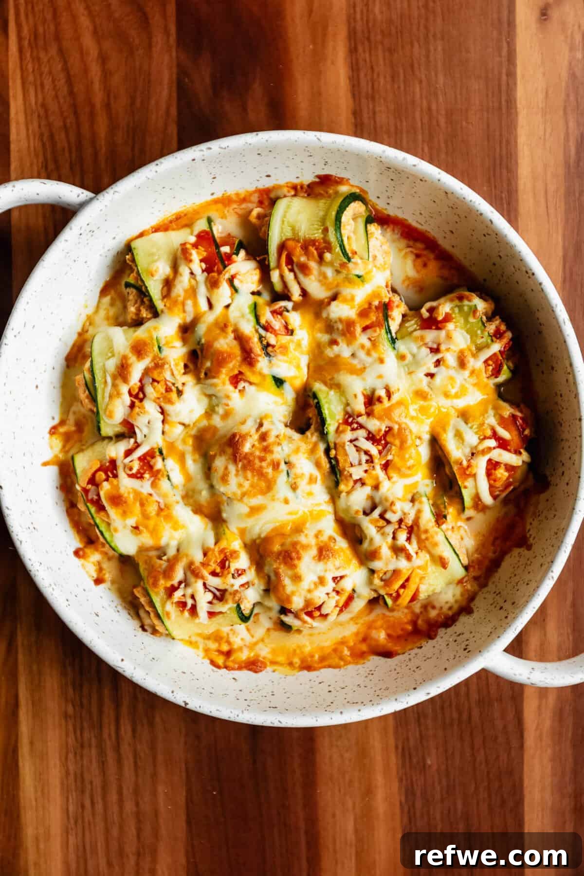 Buffalo Chicken Zucchini Roll-Ups Recipe 12 baked buffalo chicken zucchini roll ups in a baking dish with hot sauce topped with melted shredded cheeese.