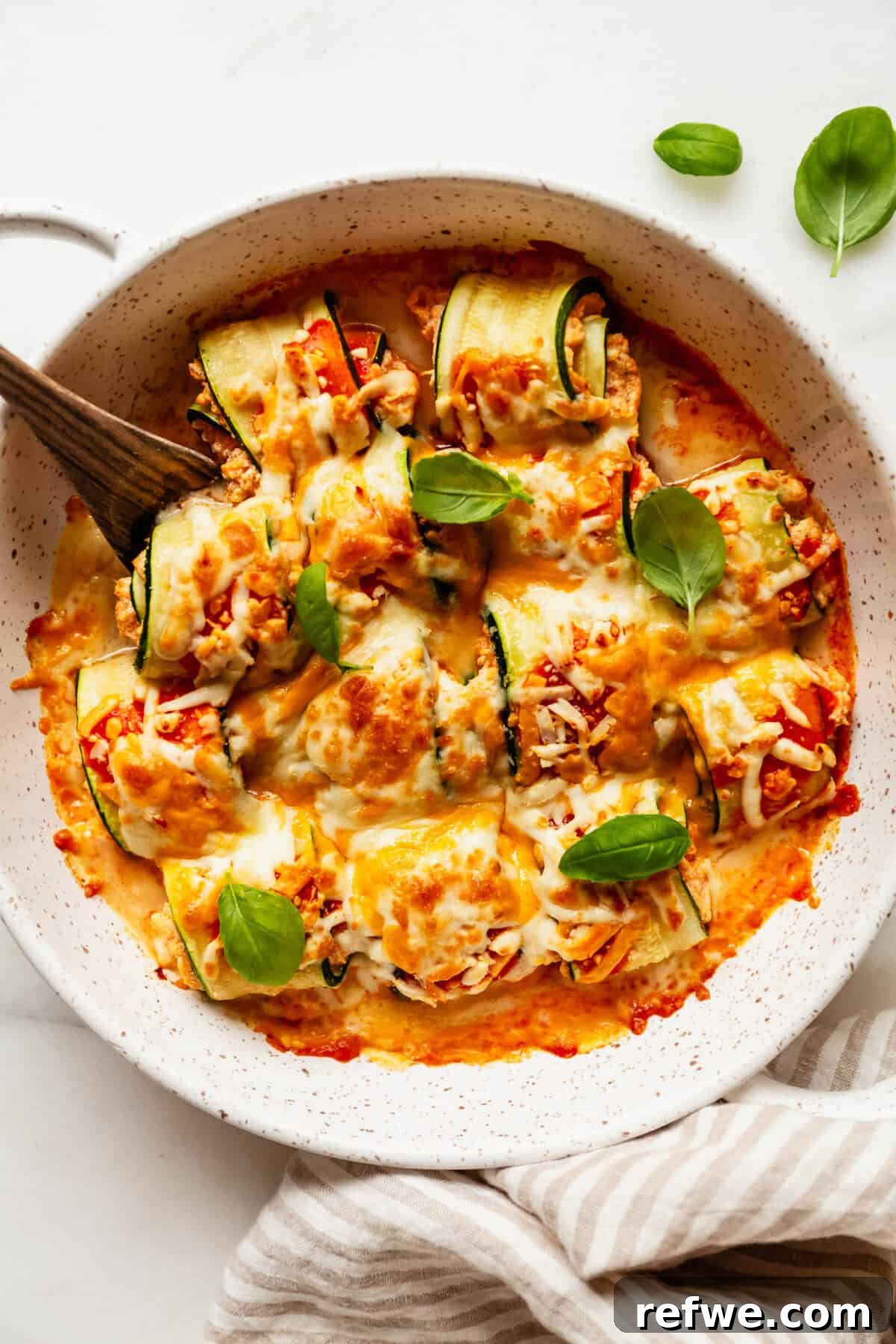 Buffalo Chicken Zucchini Roll-Ups Recipe 13 Buffalo chicken zucchini roll ups topped with basil with a wood spoon.