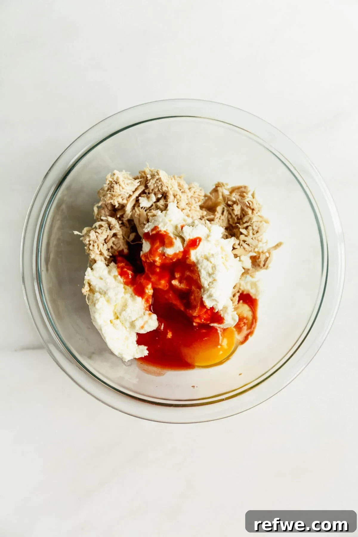 Buffalo Chicken Zucchini Roll-Ups Recipe 6 shredded chicken, egg, hot sauce and ricotta in a clear mixing bowl.